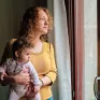 Une maman portant son bébé dans ses bras et regardant par la fenêtre de son appartement